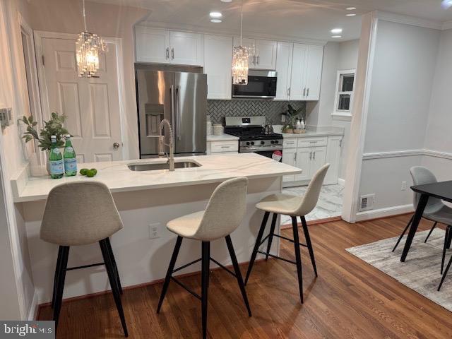 kitchen with a kitchen breakfast bar, appliances with stainless steel finishes, a peninsula, white cabinets, and a sink