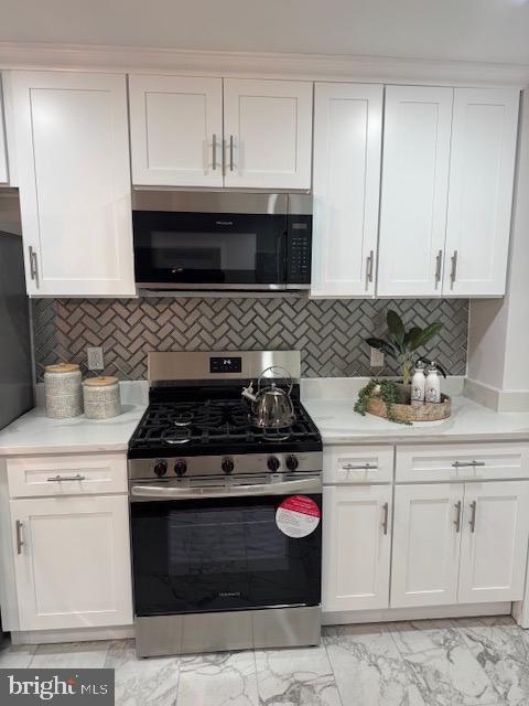 kitchen with stainless steel gas stove, marble finish floor, white cabinets, and light countertops