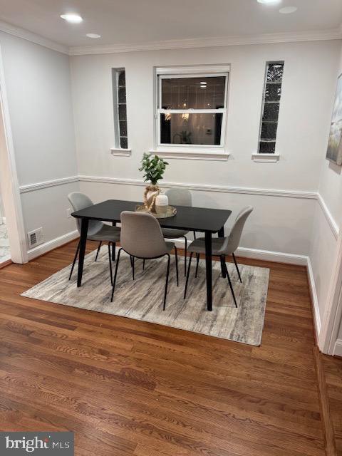 dining room with visible vents, wood finished floors, baseboards, and ornamental molding