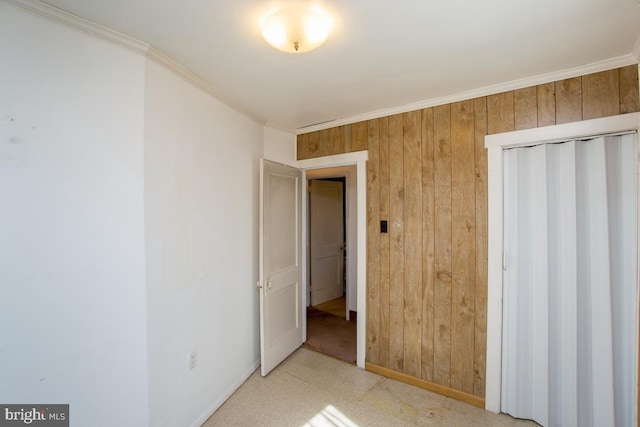 unfurnished bedroom featuring a closet, baseboards, wooden walls, and ornamental molding