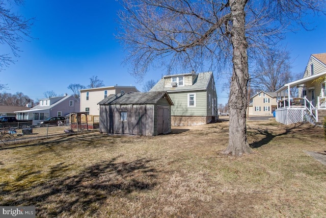 back of property featuring an outbuilding, fence, a storage unit, a lawn, and a residential view