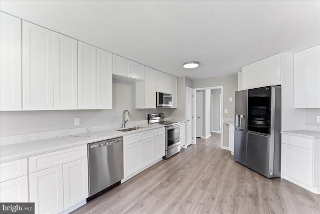 kitchen with light wood finished floors, appliances with stainless steel finishes, white cabinetry, and a sink