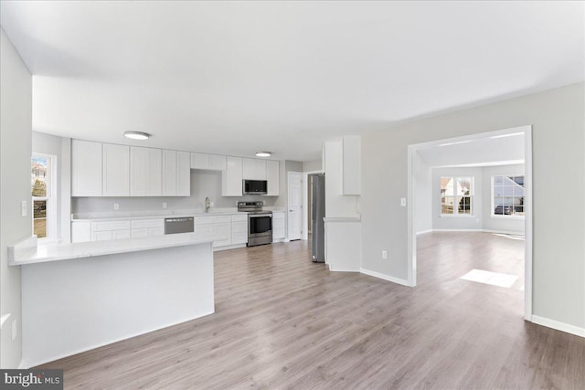 kitchen featuring baseboards, stainless steel appliances, light countertops, white cabinets, and light wood-type flooring