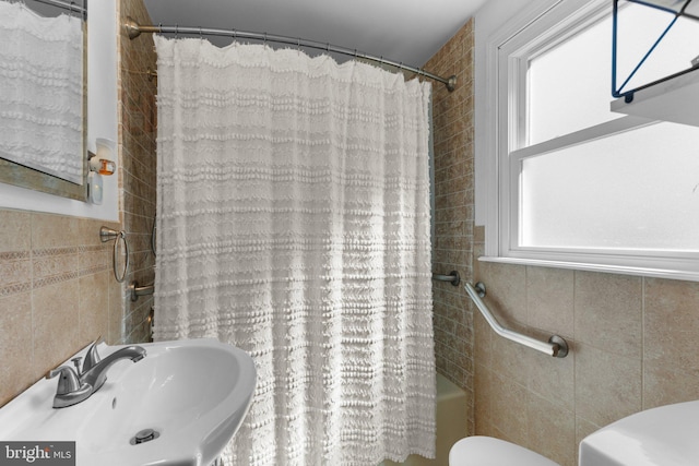 full bathroom featuring tile walls, toilet, shower / bath combo with shower curtain, and a sink