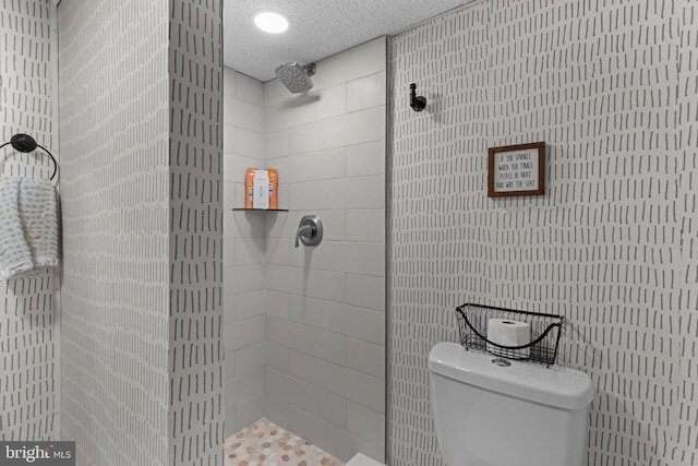 bathroom with a textured ceiling, toilet, and tiled shower