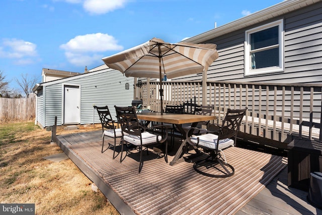 wooden terrace with an outbuilding, outdoor dining area, and fence