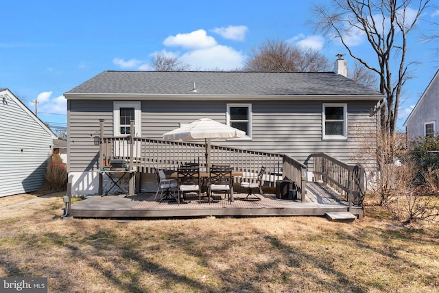 back of property featuring a wooden deck, a lawn, roof with shingles, and a chimney