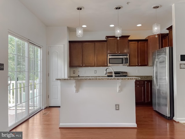 kitchen with light stone counters, plenty of natural light, wood finished floors, and stainless steel appliances