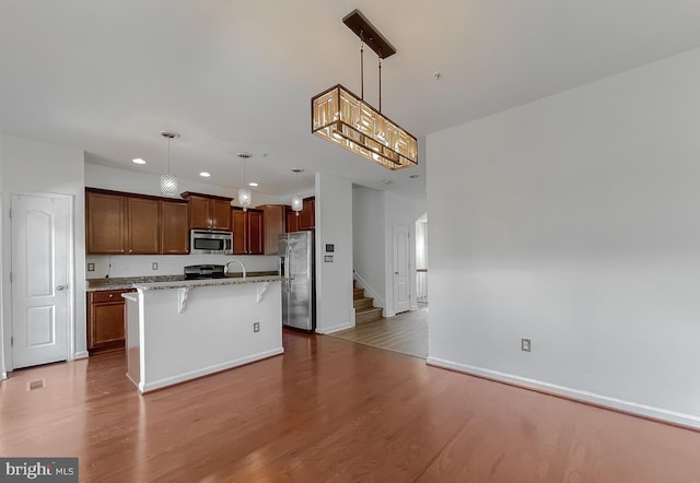 kitchen with a breakfast bar, a kitchen island with sink, wood finished floors, appliances with stainless steel finishes, and light stone countertops