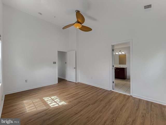 unfurnished bedroom with baseboards, visible vents, a towering ceiling, and light wood-type flooring