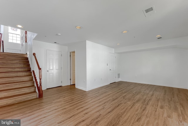 unfurnished living room featuring light wood finished floors, visible vents, stairs, and baseboards