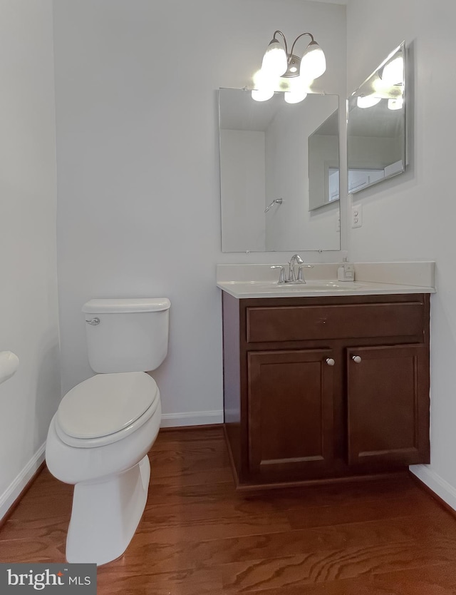 half bathroom with vanity, toilet, wood finished floors, and baseboards