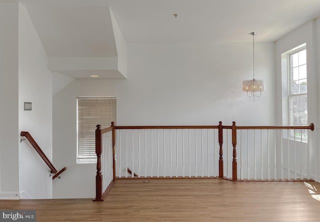 hallway with an upstairs landing, a chandelier, and wood finished floors