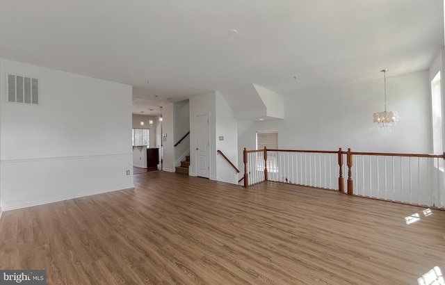 unfurnished room with a notable chandelier, visible vents, baseboards, and wood finished floors