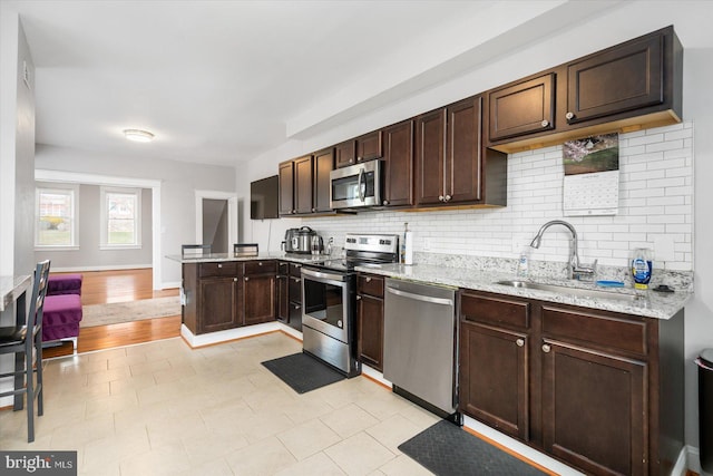 kitchen with a sink, a peninsula, stainless steel appliances, decorative backsplash, and dark brown cabinets
