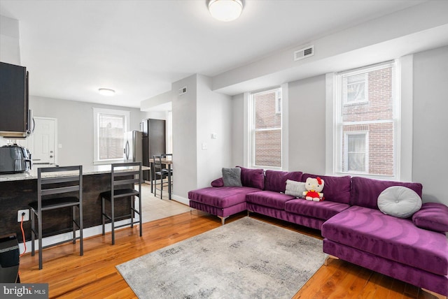 living area featuring baseboards, visible vents, light wood-type flooring, and plenty of natural light