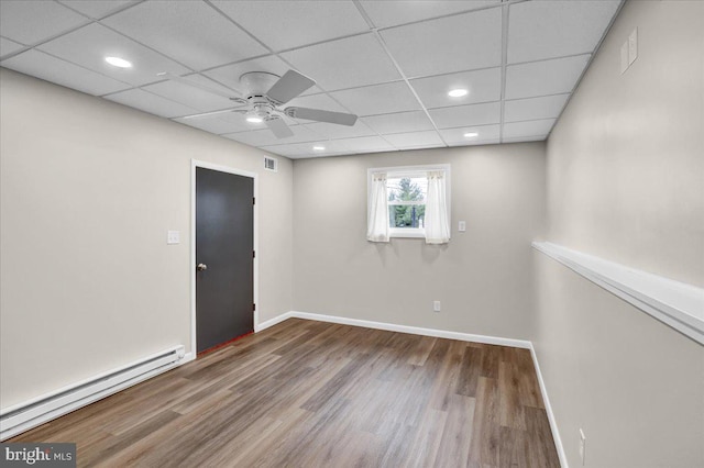 unfurnished room featuring wood finished floors, visible vents, baseboards, a baseboard radiator, and a drop ceiling