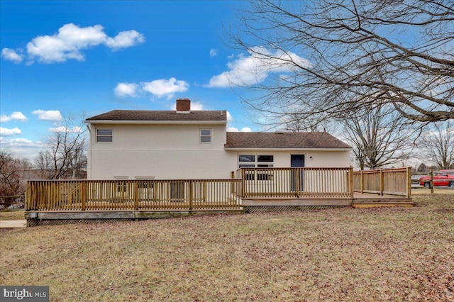 rear view of house with a lawn, a chimney, a deck, and stucco siding