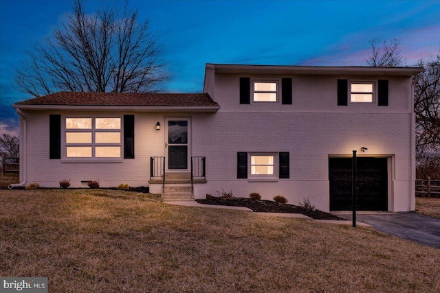 split level home featuring an attached garage, a yard, brick siding, and driveway