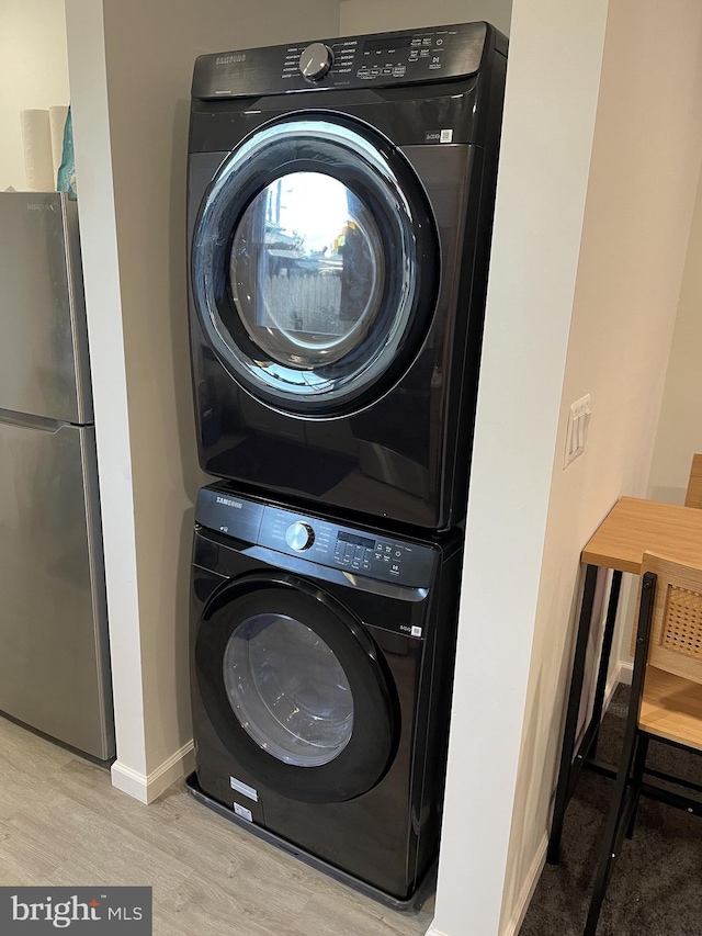 clothes washing area with baseboards, stacked washer and dryer, wood finished floors, and laundry area