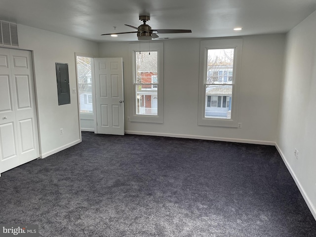 unfurnished bedroom with multiple windows, electric panel, baseboards, and dark colored carpet