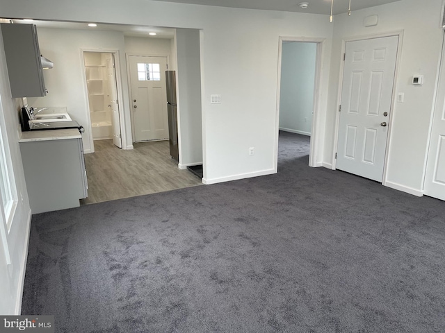 unfurnished living room with baseboards, dark colored carpet, and a sink