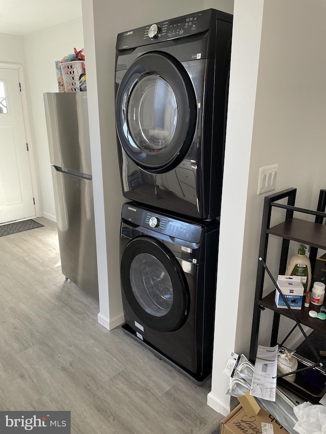 clothes washing area featuring baseboards, stacked washer and clothes dryer, wood finished floors, and laundry area