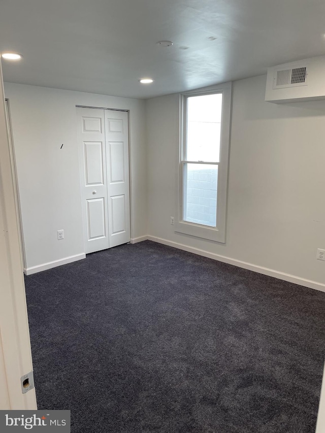 unfurnished room with dark colored carpet, visible vents, and baseboards