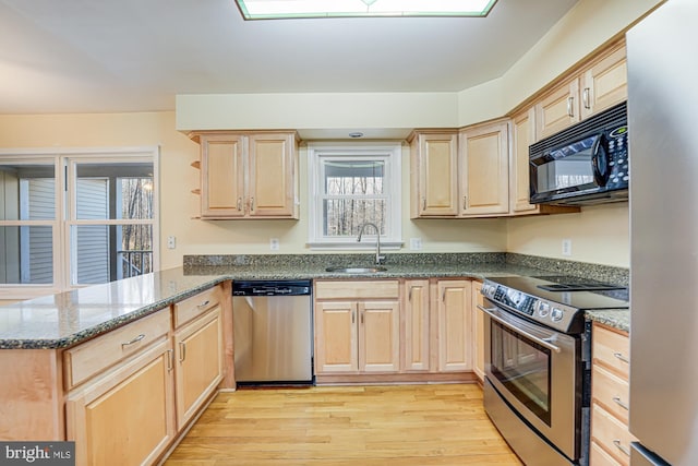 kitchen with light brown cabinets, a peninsula, a sink, light wood-style floors, and appliances with stainless steel finishes