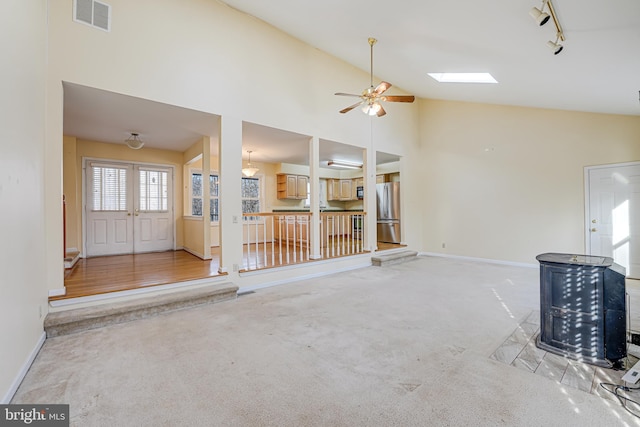 unfurnished living room with visible vents, track lighting, light carpet, a skylight, and high vaulted ceiling