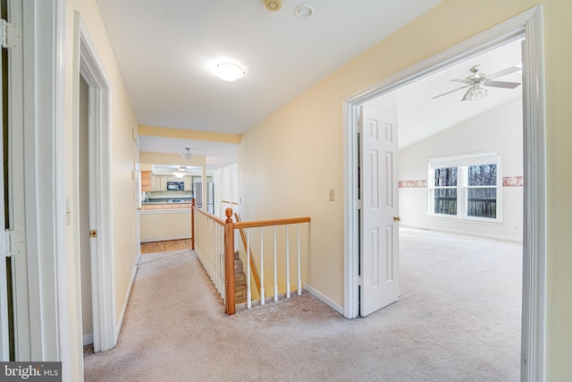 hall featuring an upstairs landing, light colored carpet, baseboards, and vaulted ceiling