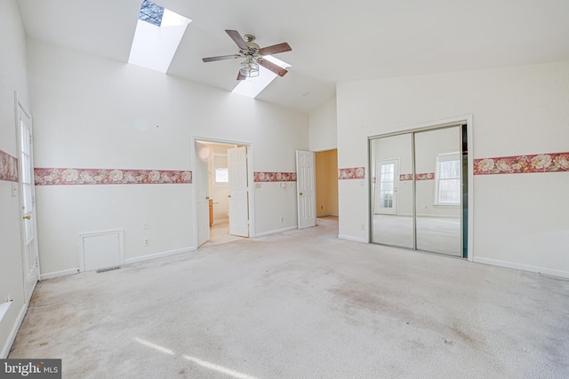 unfurnished bedroom featuring high vaulted ceiling, a closet, a skylight, carpet flooring, and baseboards