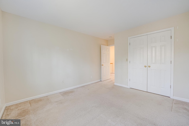 unfurnished bedroom featuring a closet, light carpet, and baseboards