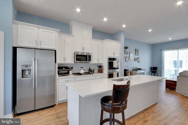 kitchen with a sink, a center island with sink, white cabinetry, and stainless steel appliances