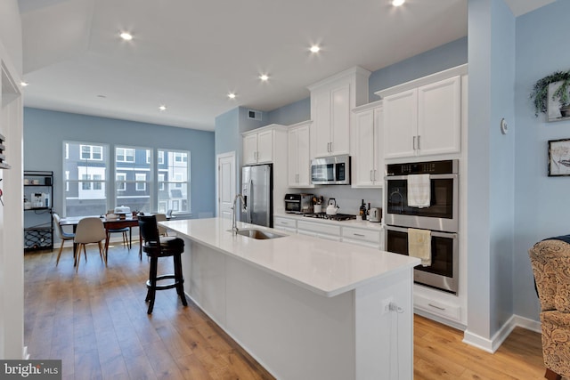 kitchen featuring light wood-type flooring, an island with sink, a sink, appliances with stainless steel finishes, and white cabinets