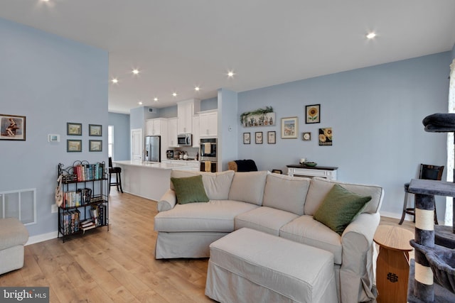 living room with light wood-type flooring, visible vents, baseboards, and recessed lighting