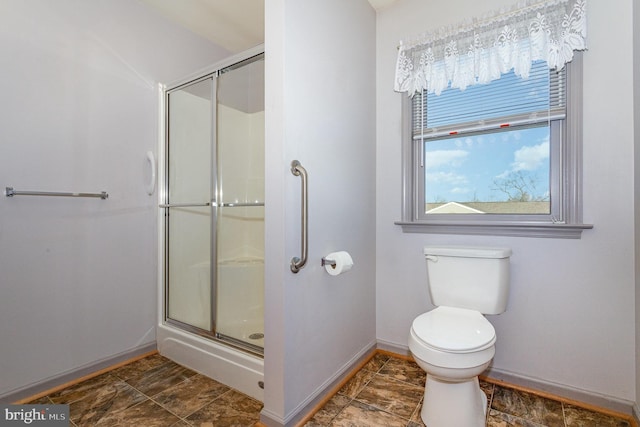 full bath featuring baseboards, toilet, a shower stall, and stone finish floor