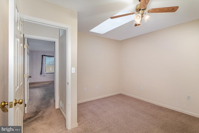 spare room with a skylight, a ceiling fan, baseboards, and light carpet