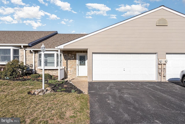 view of front of house featuring a front lawn, aphalt driveway, roof with shingles, a garage, and stone siding