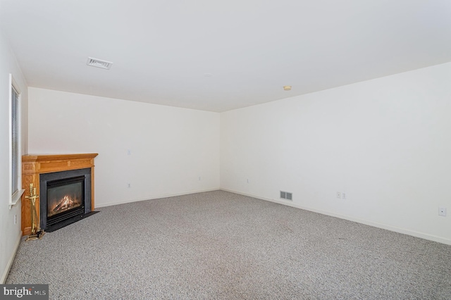 unfurnished living room featuring visible vents, a fireplace with flush hearth, baseboards, and carpet flooring