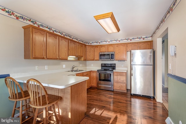 kitchen featuring dark wood-style flooring, appliances with stainless steel finishes, a peninsula, brown cabinetry, and a sink