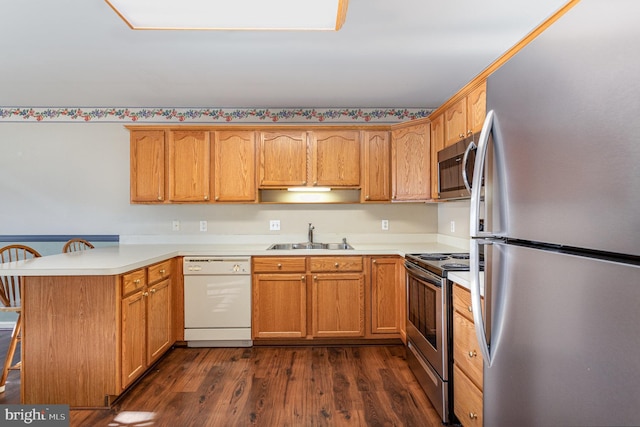 kitchen featuring dark wood finished floors, a peninsula, a sink, appliances with stainless steel finishes, and a kitchen bar