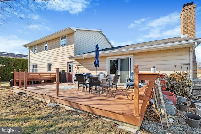 rear view of property featuring a deck, outdoor dining space, and a chimney