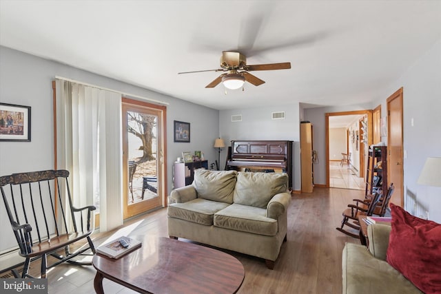 living room featuring a ceiling fan, visible vents, and light wood finished floors