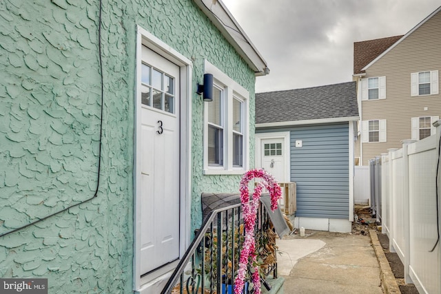 entrance to property with roof with shingles and fence