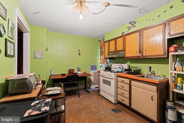 kitchen with under cabinet range hood, light countertops, white gas range, brown cabinets, and a sink