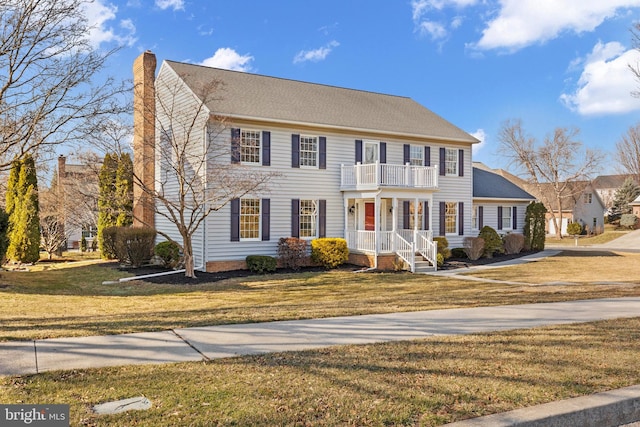 colonial-style house with a chimney, a front lawn, and a balcony