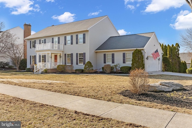 colonial home with concrete driveway, a front yard, a garage, a balcony, and a chimney