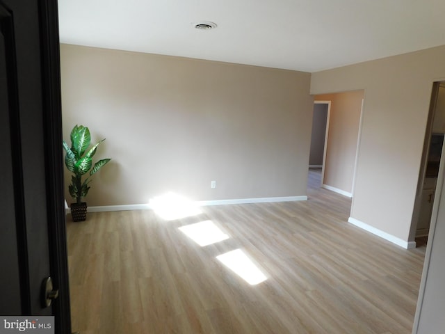 spare room with light wood-type flooring, visible vents, and baseboards