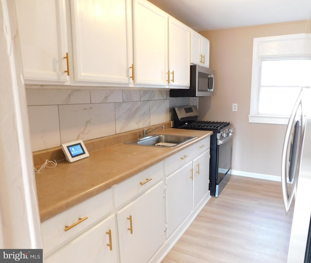 kitchen featuring backsplash, light countertops, white cabinets, stainless steel appliances, and a sink